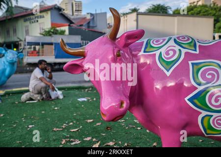 Un ouvrier de l'Inde est assis près d'une statue colorée de vache dans un petit parc. Dans la région de Little India, à Singapour, l'herbe est en fait du gazon artificiel Banque D'Images