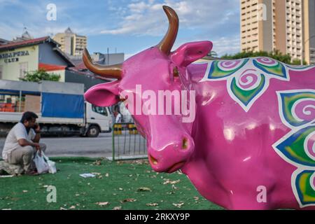 Un ouvrier de l'Inde est assis près d'une statue colorée de vache dans un petit parc. Dans la région de Little India, à Singapour, l'herbe est en fait du gazon artificiel Banque D'Images