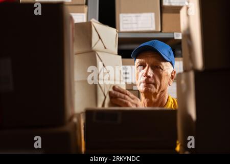 Vieux travailleur d'entrepôt prenant des boîtes en carton et des colis sur une étagère dans la salle de stockage. Banque D'Images