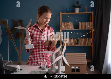 École primaire, fille tenant une tablette informatique étudiant comment les éoliennes fonctionnent travailler à la maison avec le projet. Les enfants apprennent à parler de écologique Banque D'Images