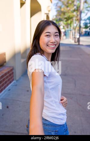 Jeune femme asiatique regardant en arrière et atteignant la main dehors pour tenir | Downtown Sidewalk Banque D'Images