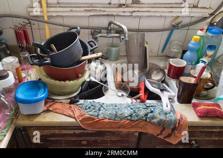 Photo en gros plan d'un évier de cuisine en désordre rempli de vaisselle et d'ustensiles sales et empilés Banque D'Images