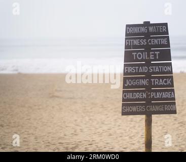 Un panneau de signalisation de plage en bois sur la rive sablonneuse : eau potable, fitness, toilettes, premiers soins, jogging tack, aire de jeux, douches et vestiaire Banque D'Images