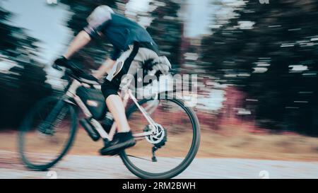 Un homme monte un vélo de bikepacking à grande vitesse sur une piste de gravier dans la forêt de Thetford dans le Norfolk, Angleterre Royaume-Uni Banque D'Images
