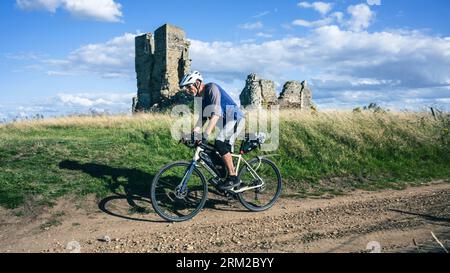 Un homme sur un voyage de bikepacking passe devant la vieille ruine de l'église de St James près de Kings Lynn dans Norfolk Angleterre Royaume-Uni Banque D'Images