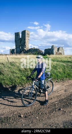 Un homme sur un voyage de bikepacking passe devant la vieille ruine de l'église de St James près de Kings Lynn dans Norfolk Angleterre Royaume-Uni Banque D'Images