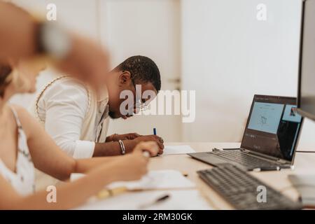 Équipe d'affaires diversifiée collaborant dans un bureau moderne - discuter des statistiques, élaborer des stratégies de croissance et partager des idées. Homme noir remplissant bu Banque D'Images
