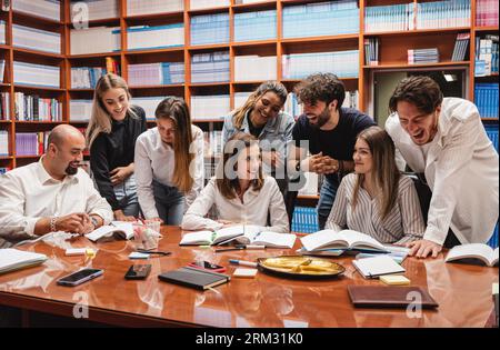 Deux professeurs et leurs étudiants rient et s’amusent dans une bibliothèque Banque D'Images