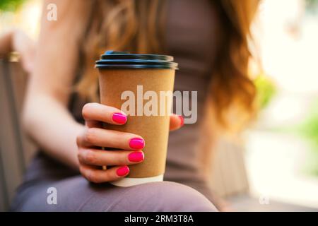 Main de femme avec une manucure brillante tenant une tasse de café recyclable à emporter à l'extérieur, les jours ensoleillés dans la ville, profitant du matin Banque D'Images