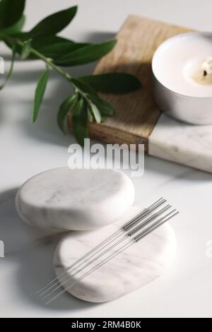 Pierres avec des aiguilles d'acupuncture sur la table blanche Banque D'Images