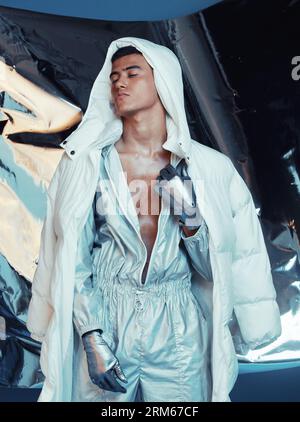 Mode, futur et cyberpunk avec un mannequin dans une tenue argentée pour une séance photo magazine en studio. Art, holographique et science-fiction avec un jeune homme Banque D'Images