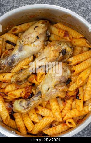 Pâtes Penne et pilons de poulet cuits dans une sauce tomate et herbes dans une casserole en acier inoxydable. Sur un fond de granit noir Banque D'Images