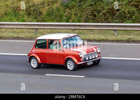 Années 1998 90 années 1990 British Orange Rover Mini Cooper travaille, rayures blanches de course ; voyageant à grande vitesse sur l'autoroute M6 dans le Grand Manchester, Royaume-Uni Banque D'Images