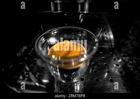 Vue de dessus d'une tasse en verre avec café noir fraîchement préparé avec de la mousse et de la crème dorée avec des bulles d'une machine à espresso entièrement automatique. Tumbl Banque D'Images