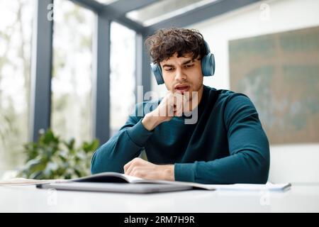 Homme européen écoutant la conférence en ligne et faisant son siège à la maison regardant attentivement dans le copybook, assis dans le public Banque D'Images