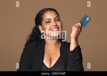 E-banking, e-commerce. Heureux latin Chubby businesswoman gérant de banque détenant la carte de crédit isolé sur fond brun Banque D'Images