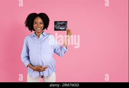 Heureuse jeune femme enceinte noire dans le ventre touchant occasionnel, profitez du dépistage, montrez l'échographie Banque D'Images