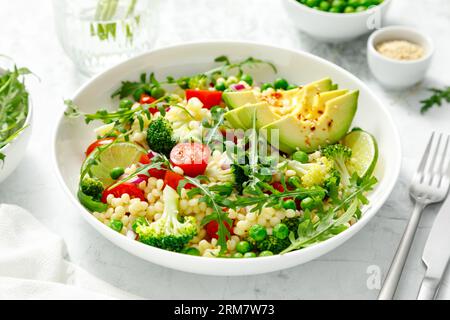 Salade de couscous avec brocoli, pois verts, tomates, avocat et roquette fraîche. Nourriture végétarienne saine à base de plantes naturelles pour le déjeuner, cuisine israélienne Banque D'Images