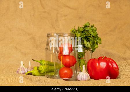 Les poivrons et l'ail et les tomates et les piments forts et les bocaux reposent sur un sac, ingrédients de cuisson pour adjika, légumes Banque D'Images