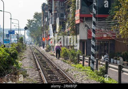 Une femme vietnamienne âgée portant un chapeau conique marche le long de la principale voie ferrée nord-sud à côté de la route 1 à Hanoi, Vietnam. C'est une journée ensoleillée Banque D'Images