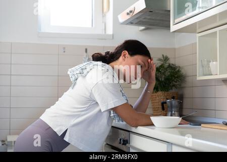 Une femme au foyer, fatiguée, frotte le poêle avec des gants. Le travail de routine domestique des femmes Banque D'Images