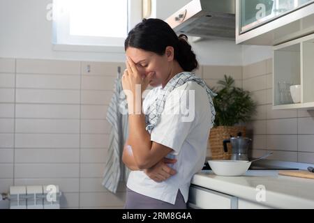 Une femme au foyer, fatiguée, frotte le poêle avec des gants. Le travail de routine domestique des femmes Banque D'Images