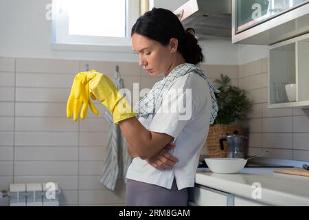 Une femme au foyer, fatiguée, frotte le poêle avec des gants. Le travail de routine domestique des femmes Banque D'Images