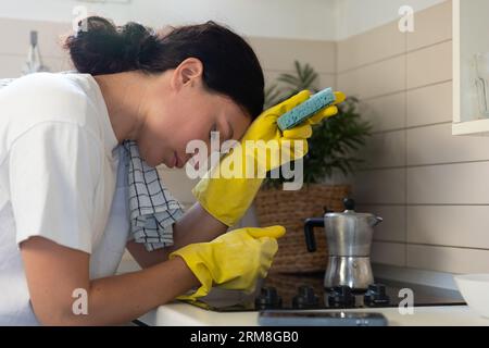 Une femme au foyer, fatiguée, frotte le poêle avec des gants. Le travail de routine domestique des femmes Banque D'Images