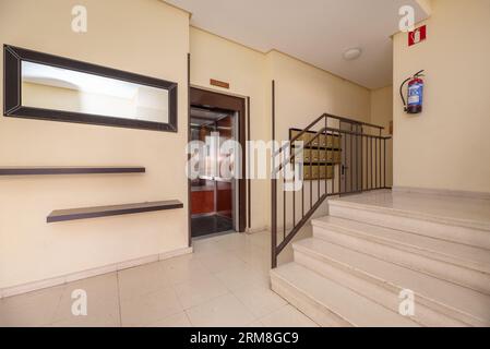 Portail d'un immeuble résidentiel avec des carreaux de terrazzo clair poli, un escalier avec une balustrade en métal brun et un ascenseur avec miroirs et W. Banque D'Images