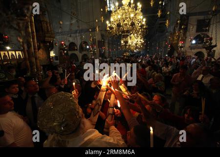 (140420) -- BETHLÉEM, 20 avril 2014 (Xinhua) - les pèlerins chrétiens touchent le feu Saint de l'église de la Nativité, construite sur le site traditionnel de la naissance de Jésus à Bethléem, le 19 avril 2014. Au cours de la cérémonie annuelle, les plus hauts clercs entrent dans l'Aédicule, la petite chambre marquant le site de la tombe de Jésus dans l'église du Saint-Sépulcre de Jérusalem, traditionnellement considérée comme le lieu de sépulture de Jésus-Christ. Ils émergent après pour révéler des bougies allumées avec le feu Saint dit être miraculeusement allumé comme un message aux fidèles du ciel. Les détails de la source de la flamme sont un guar étroitement Banque D'Images