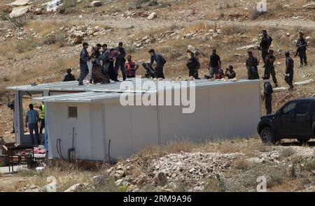 JÉRUSALEM, le 14 mai 2014 - des colons debout sur le toit de leur immeuble en signe de protestation sont arrêtés par des policiers israéliens dans la colonie de Maale-Rechavam au Nord d’Hébron, le 14 mai 2014. Mercredi, des soldats des Forces de défense israéliennes (FDI) et des forces de police ont démantelé huit bâtiments illégaux dans la colonie de Maale-Rechavam au nord d’Hébron. Le gouvernement israélien a déclaré illégaux ces bâtiments en Cisjordanie qui sont construits sur des terres palestiniennes privées et doivent être détruits. Les colons ont résisté avec des barricades et des pneus brûlés à l'entrée de la colonie comme l'armée Banque D'Images