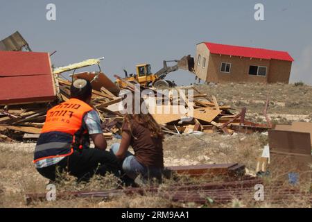 JÉRUSALEM, le 14 mai 2014 - un colon israélien (R) regarde un bulldozer de l’armée israélienne démolir un bâtiment illégal dans la colonie de Maale-Rechavam au Nord d’Hébron, le 14 mai 2014. Mercredi, des soldats des Forces de défense israéliennes (FDI) et des forces de police ont démantelé huit bâtiments illégaux dans la colonie de Maale-Rechavam au nord d’Hébron. Le gouvernement israélien a déclaré illégaux ces bâtiments en Cisjordanie qui sont construits sur des terres palestiniennes privées et doivent être détruits. Les colons ont résisté avec des barricades et des pneus brûlés à l ' entrée de la colonie comme bras Banque D'Images