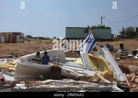 JÉRUSALEM, le 14 mai 2014 - des colons israéliens sont assis dans les restes de leur maison après qu’elle ait été démolie par un bulldozer de l’armée dans la colonie de Maale-Rechavam au Nord d’Hébron, le 14 mai 2014. Mercredi, des soldats des Forces de défense israéliennes (FDI) et des forces de police ont démantelé huit bâtiments illégaux dans la colonie de Maale-Rechavam au nord d’Hébron. Le gouvernement israélien a déclaré illégaux ces bâtiments en Cisjordanie qui sont construits sur des terres palestiniennes privées et doivent être détruits. Les colons ont résisté avec des barricades et des pneus brûlés à l'entrée de la colonie Banque D'Images