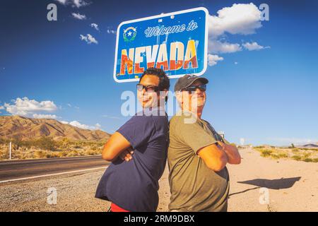 Un portrait exaltant de David et Gio Skelton, dos à dos et souriant, sous le signe « Welcome to Nevada » sur le California and Nevada Sta Banque D'Images