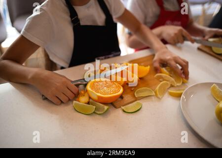 gros plan. les mains des enfants coupent des agrumes pour faire de la limonade lors d'un cours de cuisine Banque D'Images