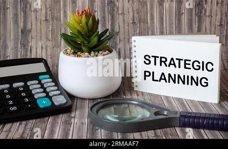 Le cahier dit planification stratégique. Calculatrice avec une loupe sur un fond en bois. Concept commercial et financier Banque D'Images