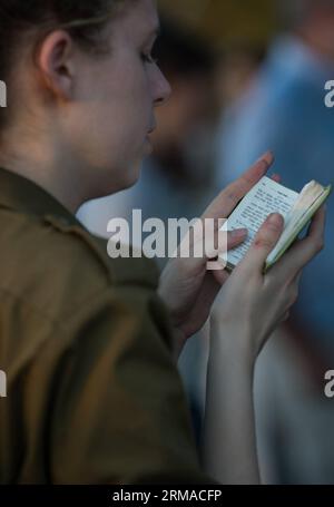 (140702) -- MODI IN, 1 juillet 2014 (Xinhua) -- une jeune femme israélienne lit la Torah lors de funérailles communes pour les trois adolescents israéliens dans un cimetière de Modi près de Jérusalem, le 1 juillet 2014. Les trois adolescents israéliens dont les corps ont été retrouvés lundi soir ont été mis au repos côte à côte mardi lors d’funérailles communes tenues à Modi, près de Jérusalem. Des dizaines de milliers de personnes ont participé aux funérailles, dont le Premier ministre Benjamin Netanyahu et le président Shimon Peres, qui ont fait l’éloge des trois, dont les cercueils étaient enveloppés de drapeaux israéliens. (Xinhua/Li Rui)(ctt) T-shirt MIDEAST-MODI IN-THREE ISRAELI Banque D'Images