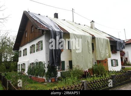 Bad Bayersoien, Allemagne. 27 août 2023. Après la tempête dans le quartier de Garmisch-Partenkirchen, le toit d'un immeuble résidentiel est provisoirement recouvert de bâches. En raison de graves dégâts causés par la tempête, le bureau de district de Garmisch-Partenkirchen a déclaré dimanche une situation catastrophique pour la ville, qui compte environ 1 300 habitants. 80 % des bâtiments de la ville seraient gravement endommagés. Crédit : Felix Hörhager/dpa/Alamy Live News Banque D'Images