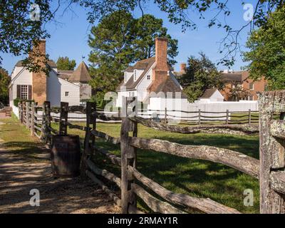 Une clôture en bois et un tonneau menant à des maisons coloniales blanches sous un ciel bleu clair à Williamsburg, en Virginie. Banque D'Images