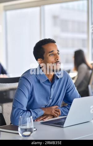 Homme d'affaires africain réfléchi assis au travail avec l'ordinateur portable regardant loin. Banque D'Images