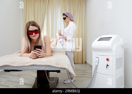 Au salon de beauté, la femme se détend pendant la session d'épilation de laser sur ses jambes Banque D'Images