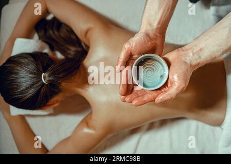 Homme de masseuse bol de maintien avec huile chaude infusée aux herbes pour le massage du dos Banque D'Images