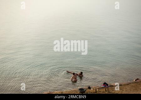 Les touristes couverts de boue nagent dans la mer Morte, Jordanie Banque D'Images