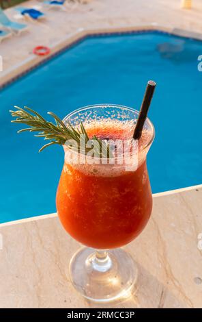 Verre de cocktail smoothie au jus de fraise avec paille contre une piscine lagon bleu Banque D'Images