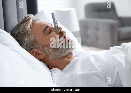 Homme dormant avec des épingles à linge sur son nez dans le lit à la maison. Problème de ronflement Banque D'Images