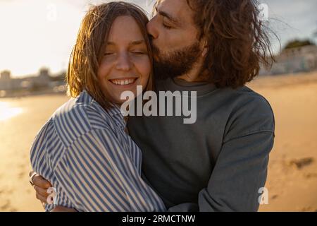 Gros plan de couple amoureux embrassant et embrassant tout en marchant le long de la plage par jour ensoleillé venteux Banque D'Images