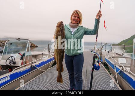 Heureuse pêcheuse tenant une grosse morue arctique. Norvège pêche heureuse. Femme avec du poisson de morue dans les mains Banque D'Images