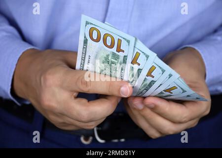 Dollars AMÉRICAINS dans la main masculine de près, l'homme en vêtements d'affaires tient l'argent. Concept de pot-de-vin, salaire, aide financière ou prêt Banque D'Images