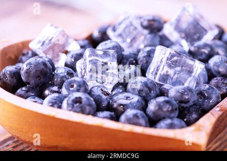 Myrtilles fraîchement cueillies avec des glaçons dans une assiette en bois en forme de cœur. Banque D'Images