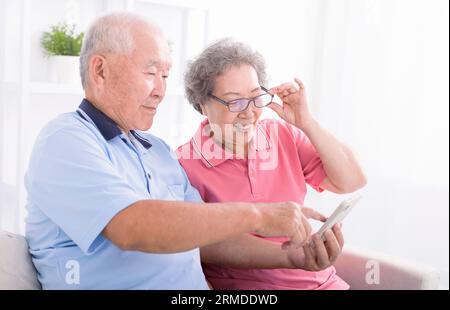Heureux couple senior utilisant le téléphone cellulaire ensemble à la maison, surfer sur Internet, assis sur le canapé Banque D'Images